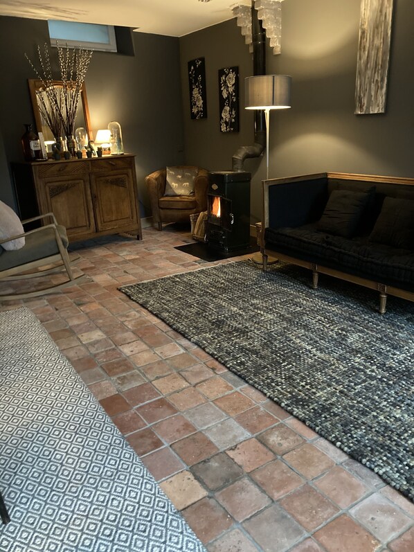 A cozy living room with a fireplace, a sofa, a patterned rug, and a wooden cabinet. - Le Pigeonnier (Croix)