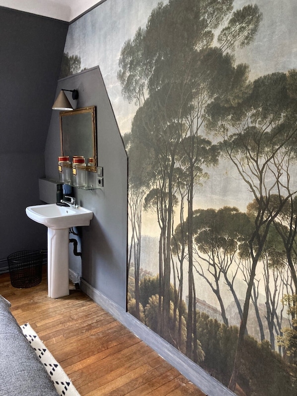 Une salle de bain avec un lavabo blanc, un miroir et une grande fresque représentant une forêt sur le mur.