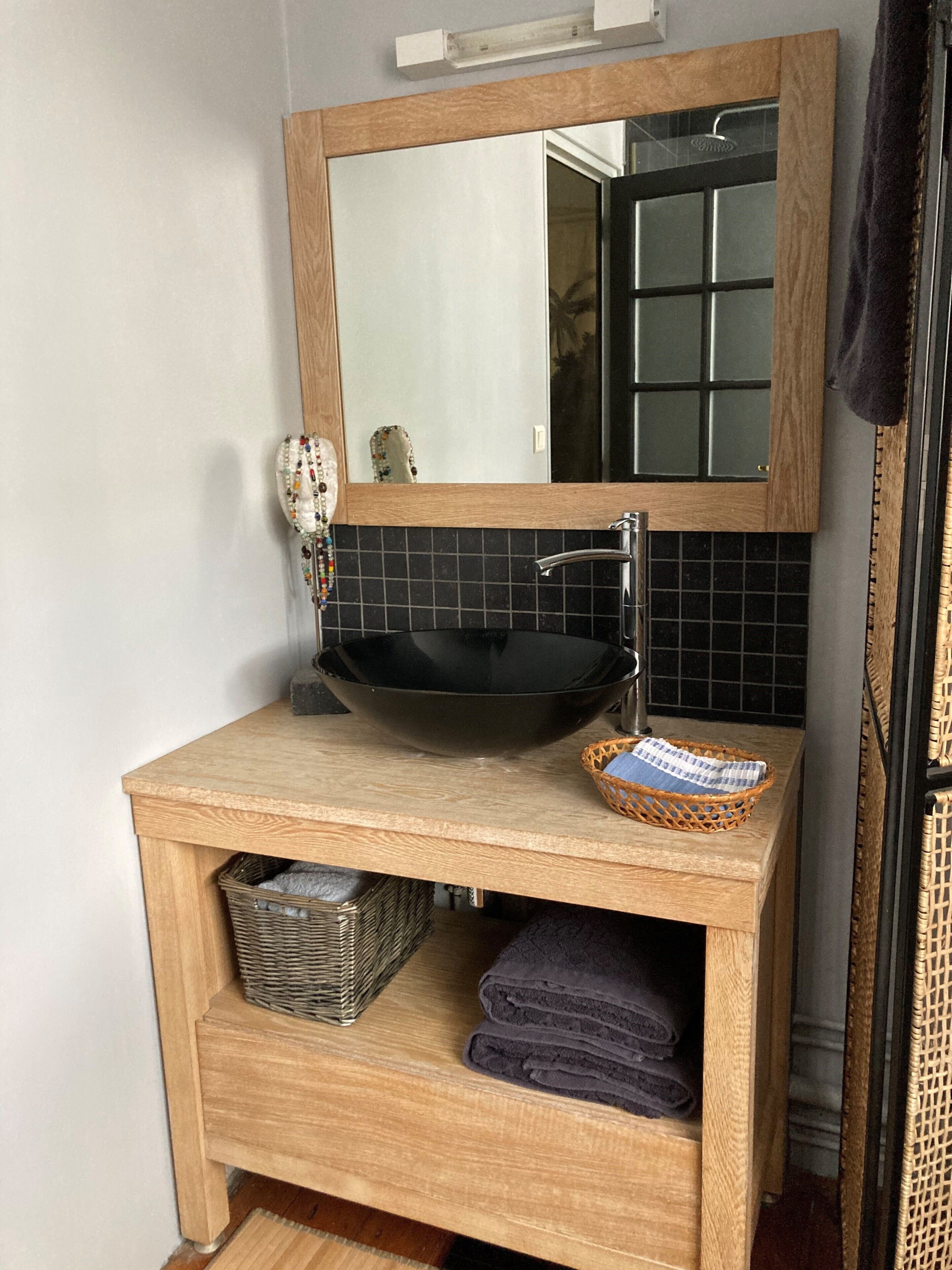 A wooden vanity with a black sink, a mirror, and a wicker basket.