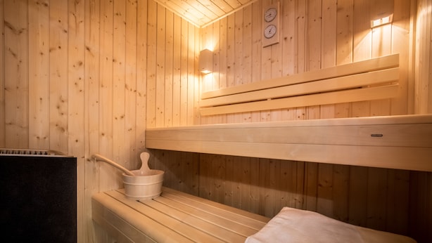 Uma sala de sauna com bancos de madeira, um banco com toalha e um aquecedor.