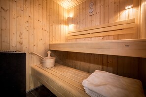 A sauna room with wooden benches, a bench with a towel, and a heater. - Le Pigeonnier (Croix)