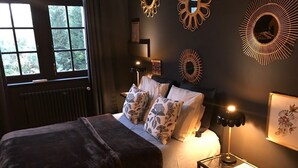 Quarto com cama, luminárias de cabeceira, mesa de apoio e espelhos decorativos na parede.