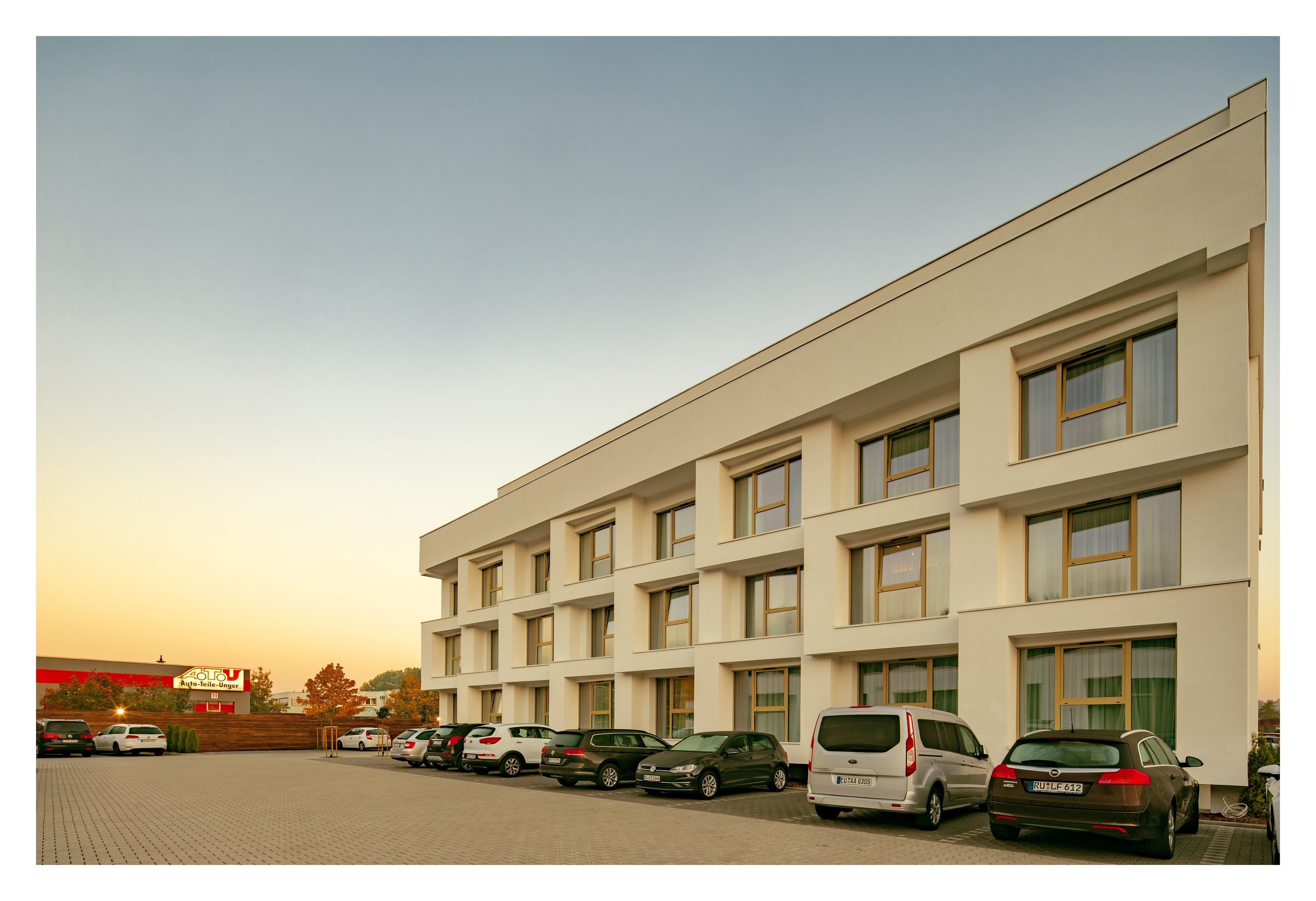 Un bâtiment moderne doté de nombreuses fenêtres et d’un parking où sont garées plusieurs voitures.