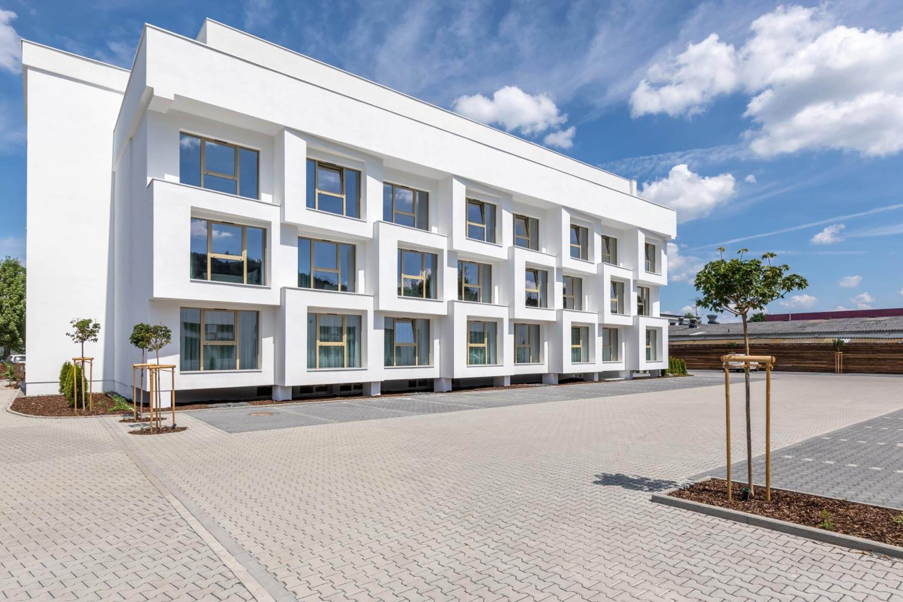 Un edificio moderno con techo plano, varias ventanas y un patio empedrado.