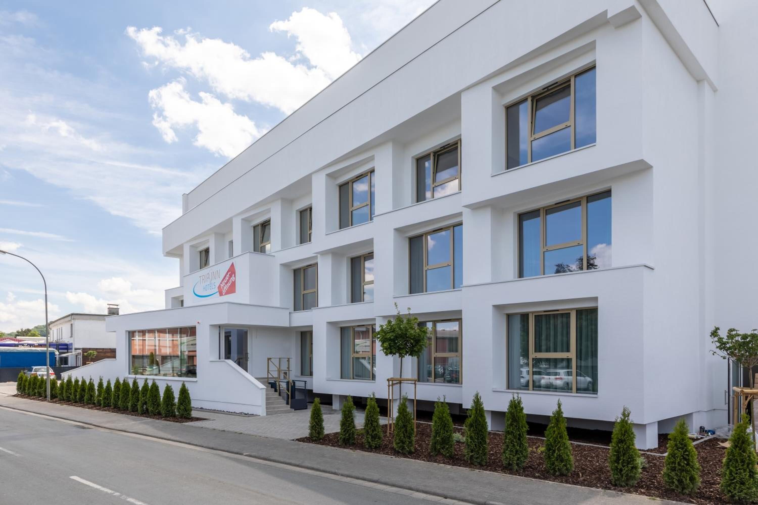A modern hotel building with a white facade, multiple windows, and a visible entrance with steps.