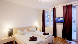 A hotel room with a bed, bedside tables, a TV, and a window with curtains. - Ferienwohnungen Eicher Fritz Reuter Straße (Rostock)