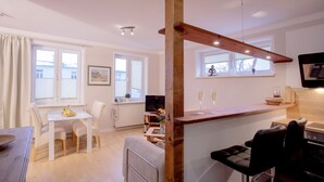 A modern kitchen with a wooden beam structure, a dining area with white chairs, and a view of the outside through large windows. - Ferienwohnungen Eicher Fritz Reuter Straße (Rostock)