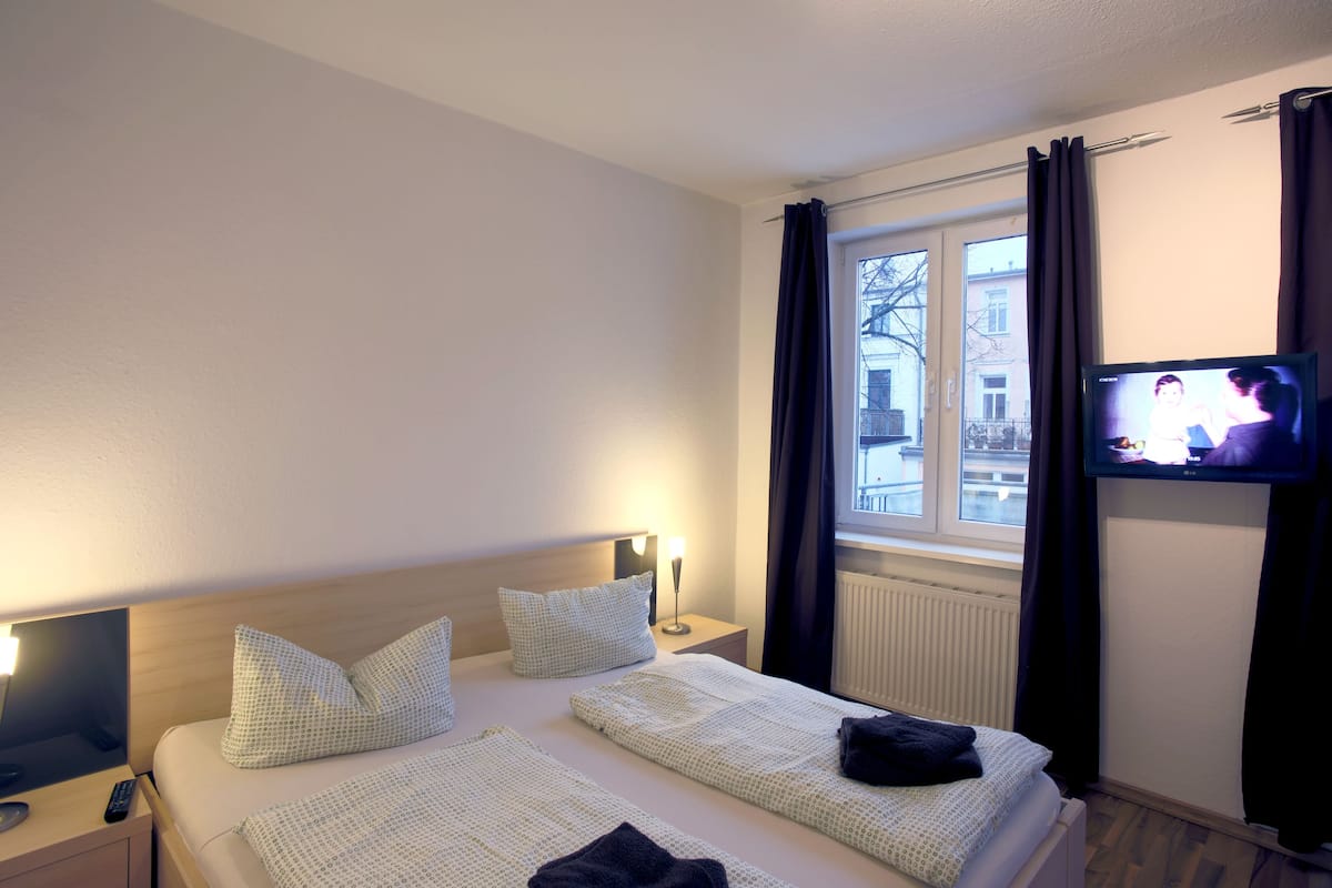Une chambre d’hôtel avec deux lits, un téléviseur fixé au mur et une fenêtre avec des rideaux.