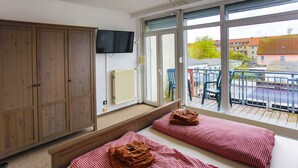 A room with two beds, a wooden wardrobe, a television, and a balcony with chairs and a railing. - Ferienwohnungen Eicher Fritz Reuter Straße (Rostock)