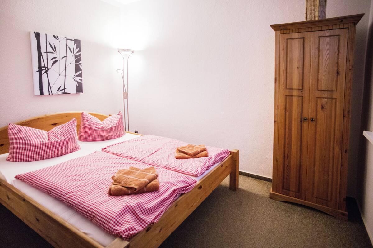 Une chambre à coucher avec un lit en bois, une literie à carreaux, une lampe de chevet et une armoire.