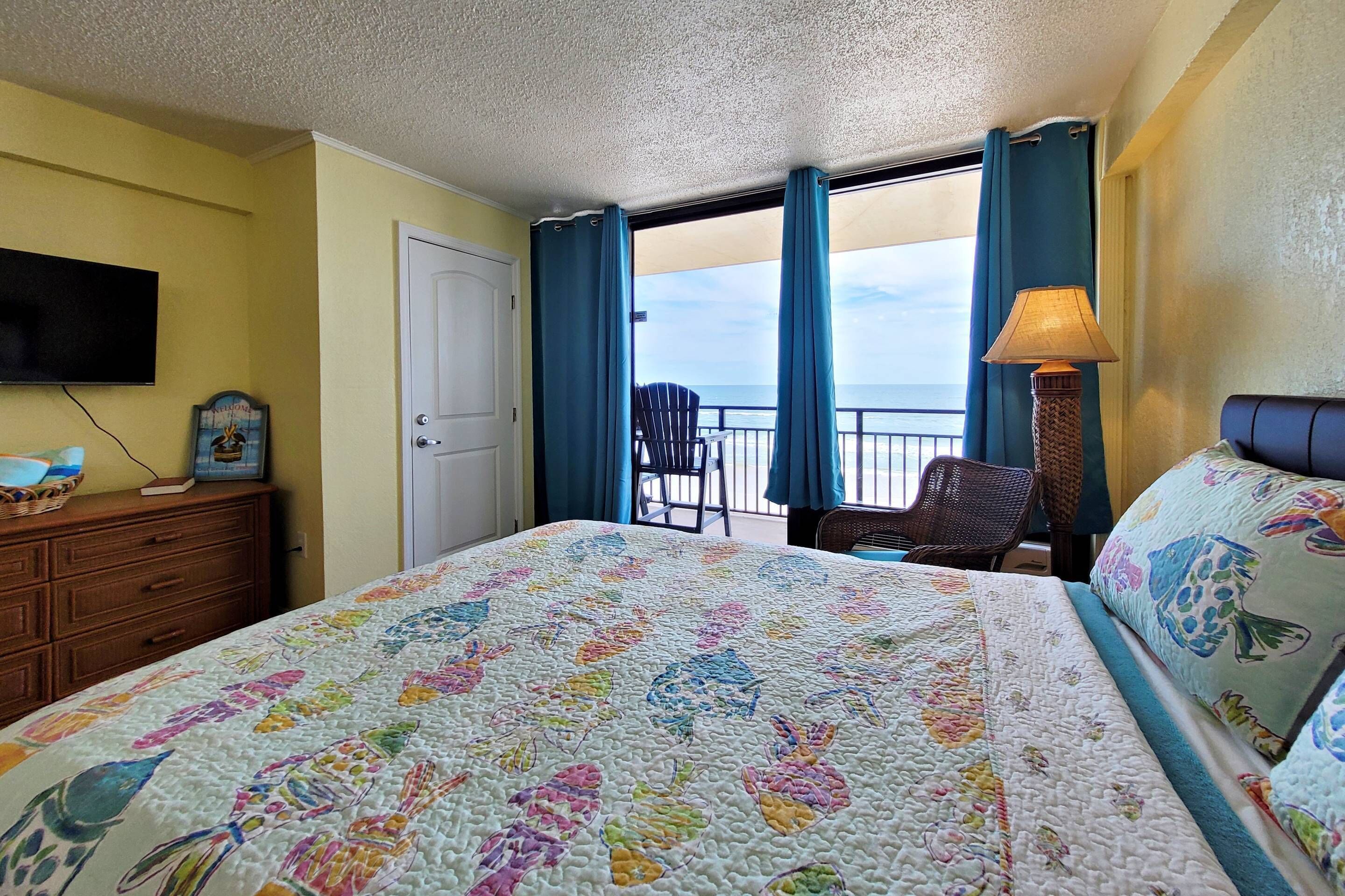 Habitación de hotel con cama, televisión, cómoda, una silla y vista al océano.