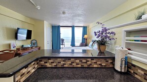 Habitación de hotel con cocina, una mesa de comedor, televisión y vistas al océano.