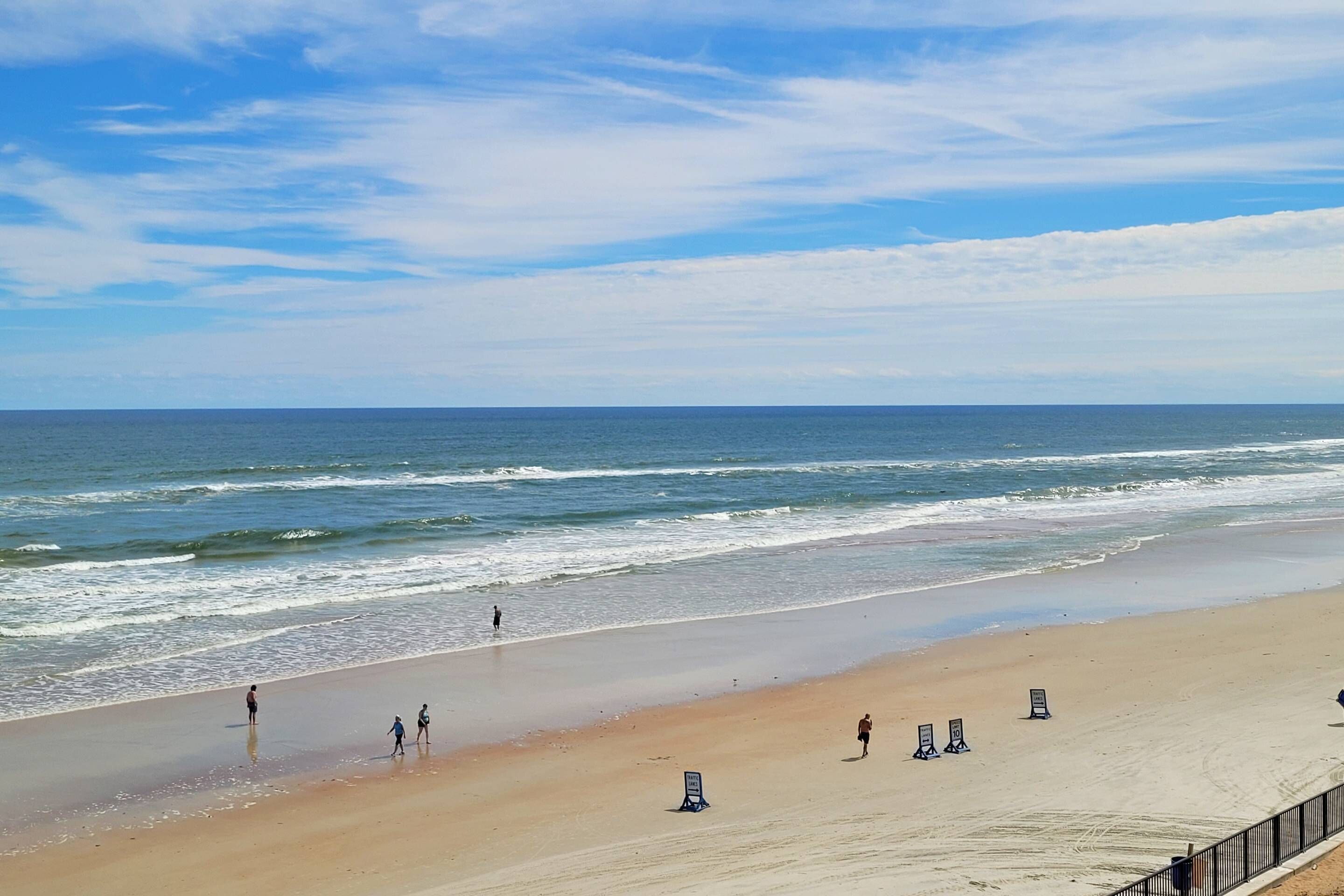 Une plage avec un rivage sablonneux, quelques personnes qui se promènent et un ciel dégagé.