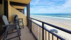 Un balcón con vistas a la playa, una silla, una mesa y un coche aparcado en la arena.