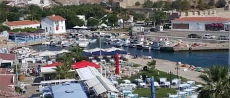 Un pueblo costero con un castillo histórico, un puerto deportivo con barcos y terrazas al aire libre.