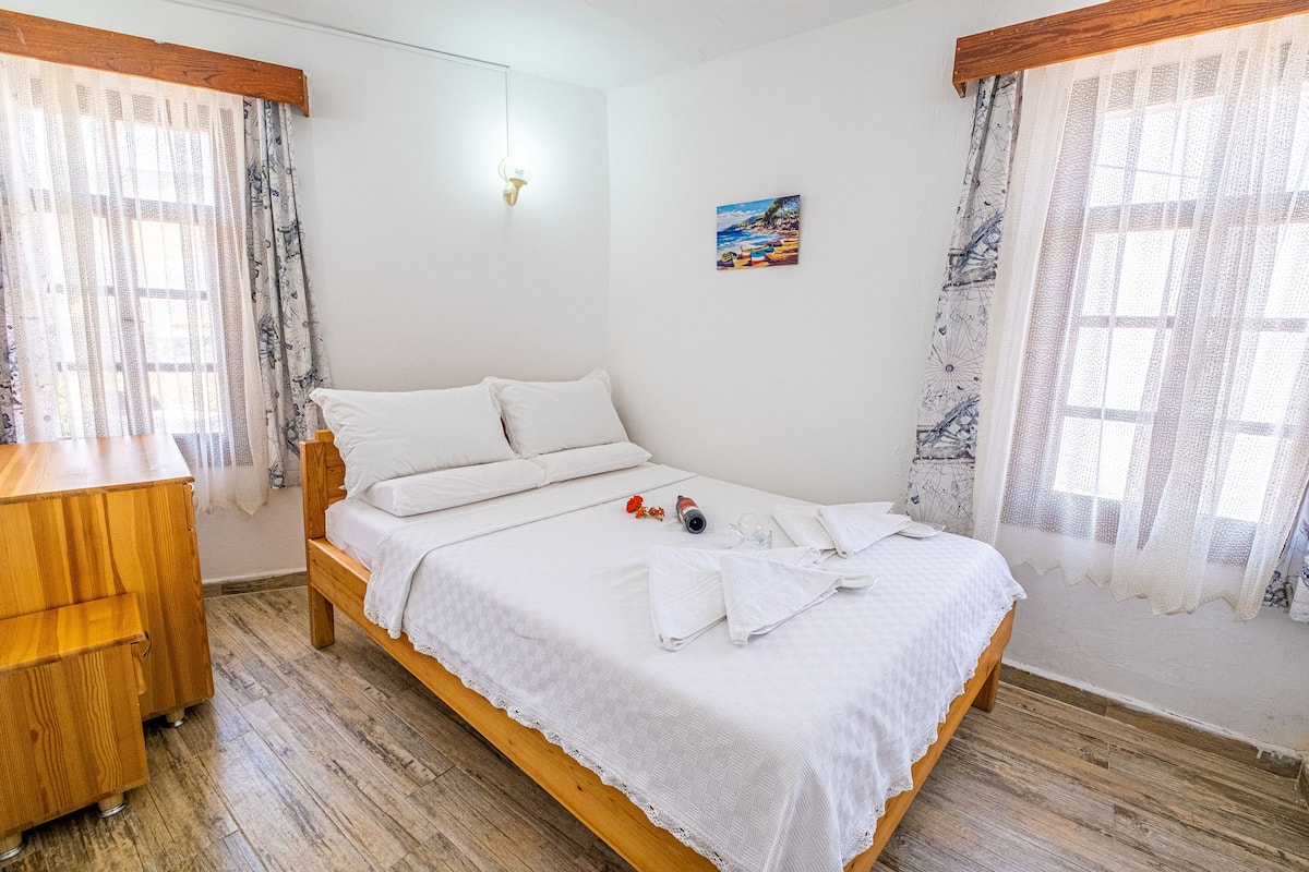 Una cama bien hecha con sábanas blancas, un aparador de madera y un cuadro en la pared.