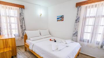 A neatly made bed with white linens, a wooden dresser, and a painting on the wall.
