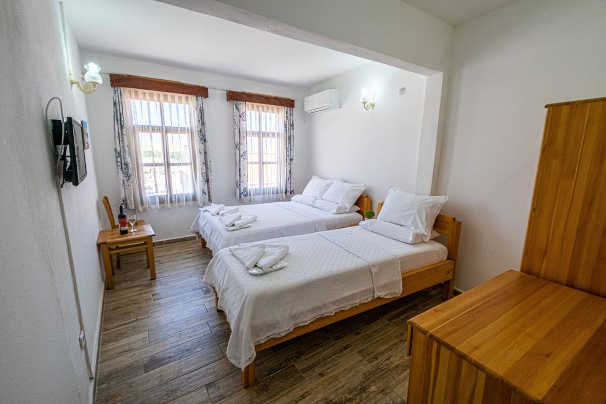Una habitación con dos camas, suelo de madera, una mesita y una silla.