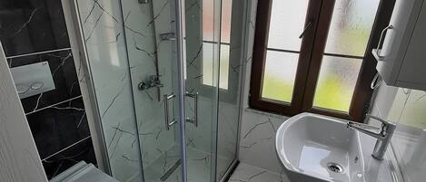 A modern bathroom with a glass-enclosed shower, a white sink, and a toilet.