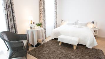 Ein Schlafzimmer mit einem großen Bett, einem Nachttisch mit Lampe, einem kleinen runden Tisch ebenfalls mit Lampe, einem Sessel und einem Teppich.