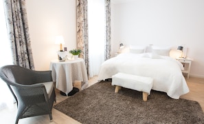 A bedroom with a large bed, a bedside table with a lamp, a small round table with a lamp, a chair, and a rug.
