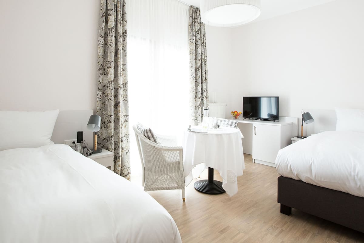 A hotel room with two beds, a small table, a chair, a TV, and a desk with a lamp.
