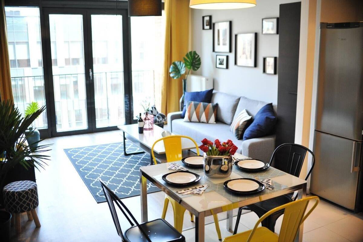Uma sala de estar moderna com sofá, mesa de jantar, cadeiras e área de cozinha com geladeira.