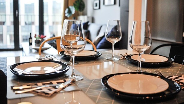 A dining table set with plates, cutlery, and wine glasses, with a modern interior and a view of the city. - 3D Szlak Apartament (Kraków)
