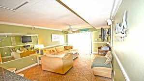 A living room with a sofa, a small table, a television, and a ceiling fan. - Seatime 303S-Oceanside 136th St, Free WiFi, Pool, Elev, W/D, AC (Ocean City)
