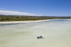 A boat on a clear, shallow beach with a forested background and distant buildings. - Dunsborough Cottage in Peron Ave (Dunsborough)