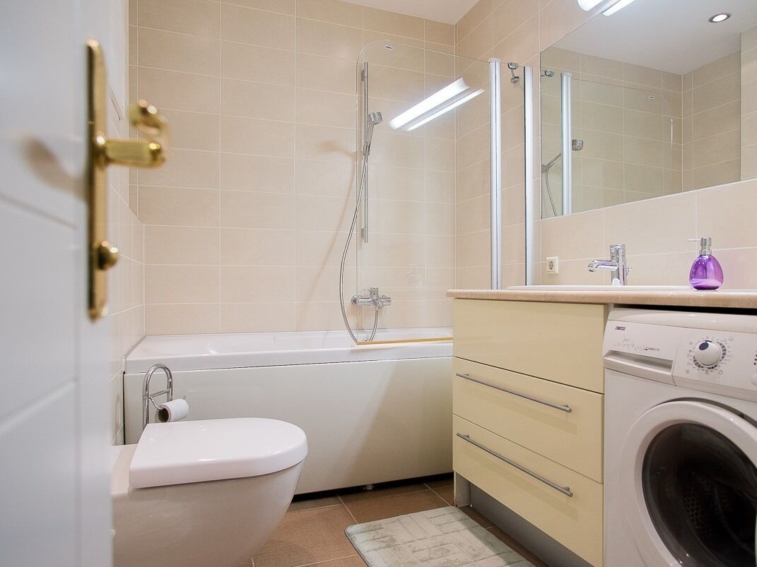 A modern bathroom with a toilet, bathtub, shower, and washing machine.