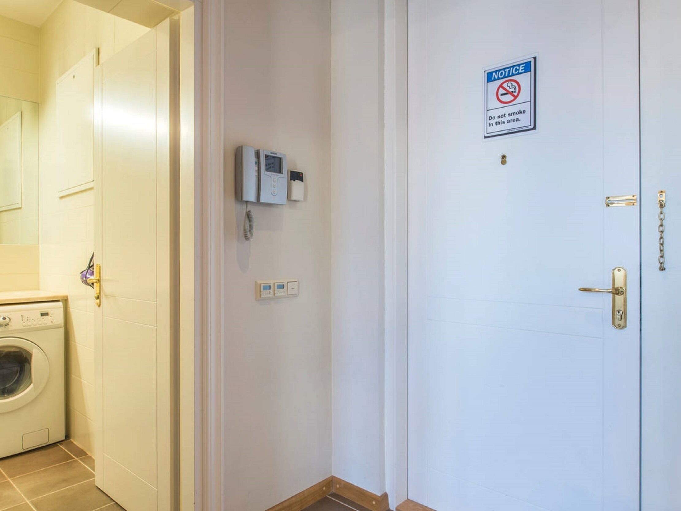 A hotel room with a washing machine, a door with a 'No Smoking' sign, and a security intercom system.