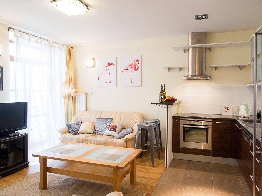 A modern living room with a sofa, coffee table, and TV. It includes a kitchen with a stove and cabinets.