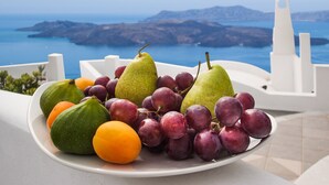A plate of fruits with a scenic view of a coastal landscape in the background. - Amity Suites - Adults Only (Santorini)