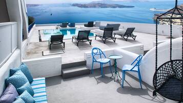 A terrace with a pool, lounge chairs, and a hanging chair overlooking the sea.