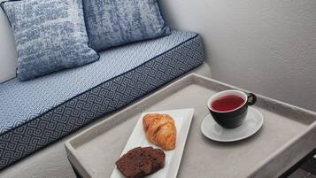 A tray with a croissant, a chocolate piece, and a cup of tea on a table next to a sofa with patterned cushions.