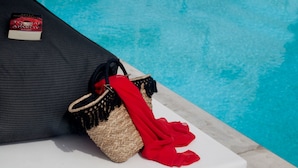 A poolside area with a woven basket and a red cloth, and a book titled "To Kill a Mockingbird" on a cushion. - Amity Suites - Adults Only (Santorini)