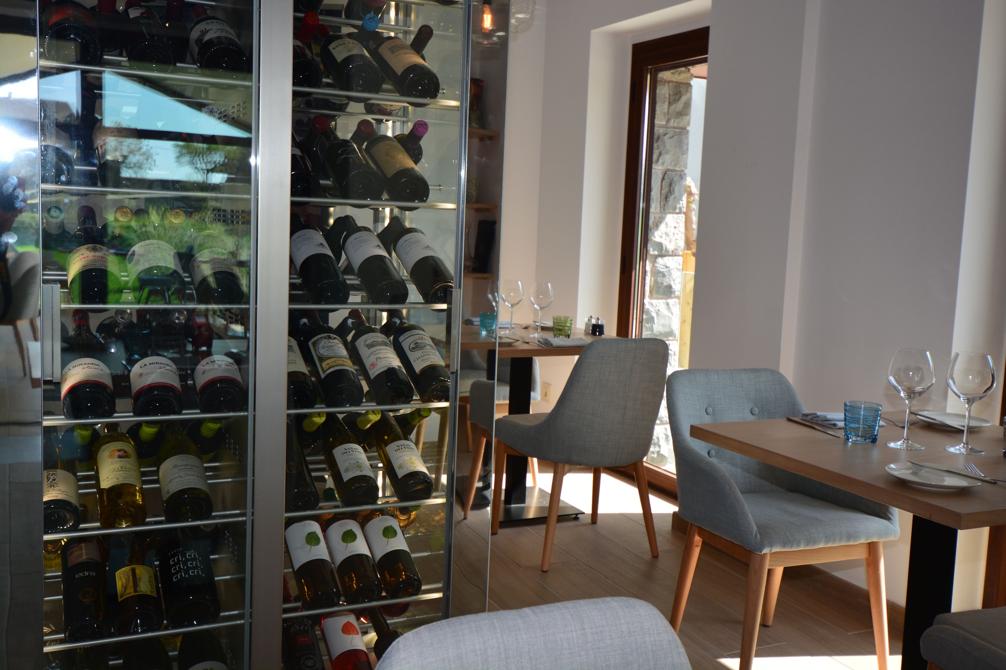 A dining area with a glass wine rack, a table set for two, and a chair.