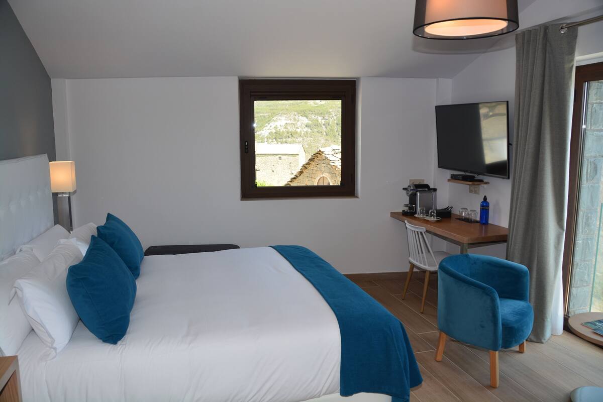 Hotelkamer met een bed, bureau, stoel, televisie en raam met uitzicht op een berg.