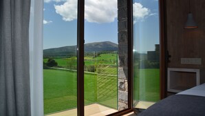 Ein Zimmer mit einer großen Glastür, die auf einen Balkon mit herrlichem Blick auf grüne Felder und Berge führt.