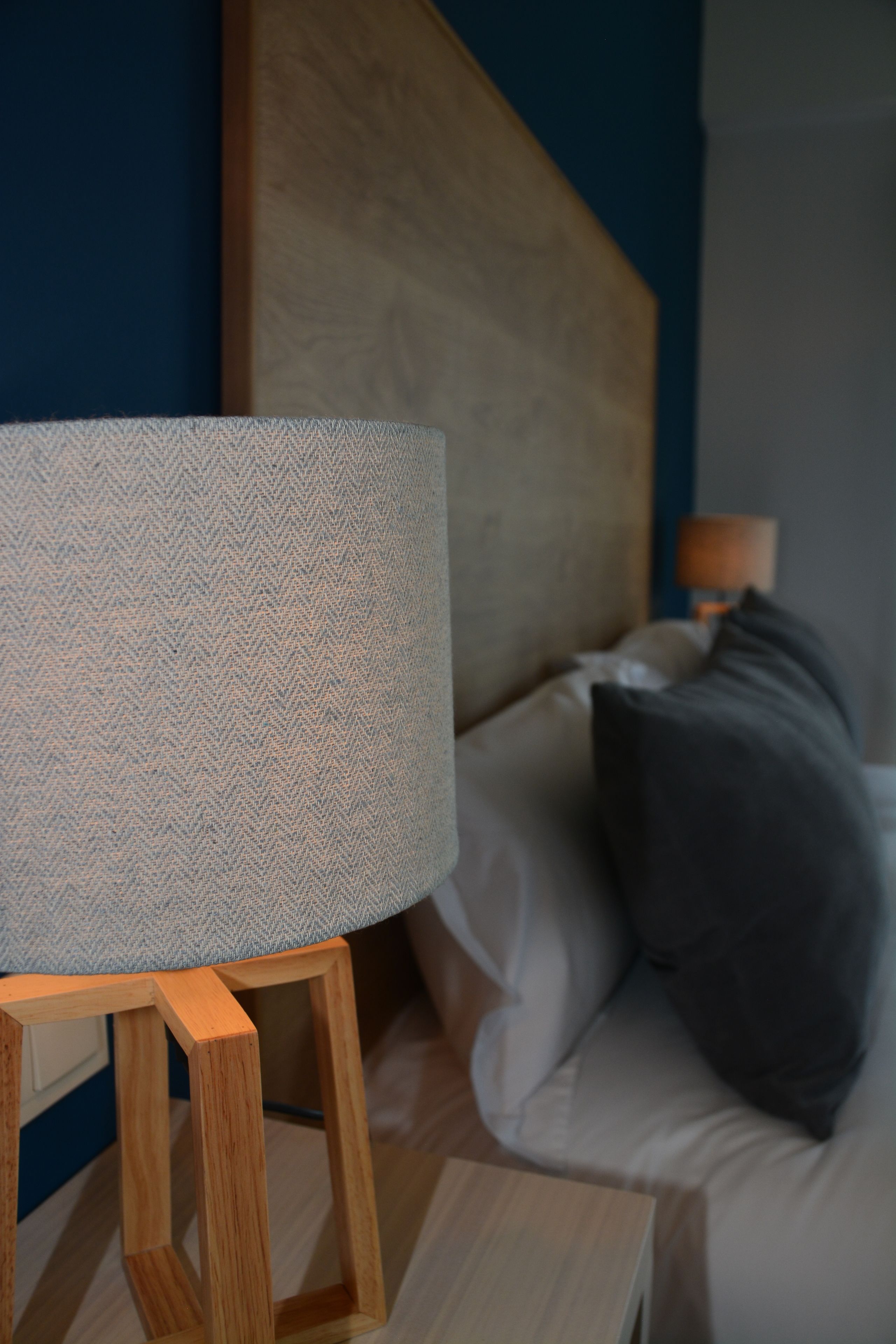 A bed with a wooden headboard, a bedside table with a lamp, and a patterned throw on the bed.