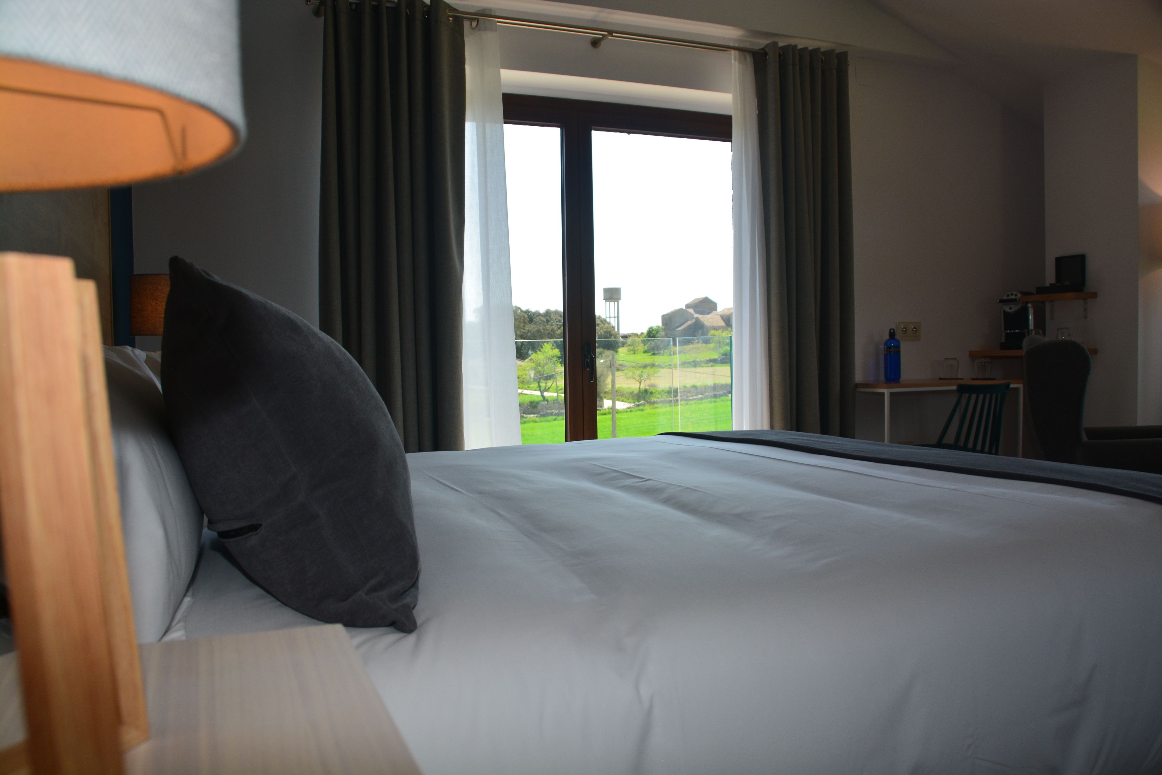 Een hotelkamer met een groot bed, een bureau en uitzicht op een groen landschap door een schuifdeur.