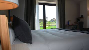 Een hotelkamer met een groot bed, een bureau en uitzicht op een groen landschap door een schuifdeur.