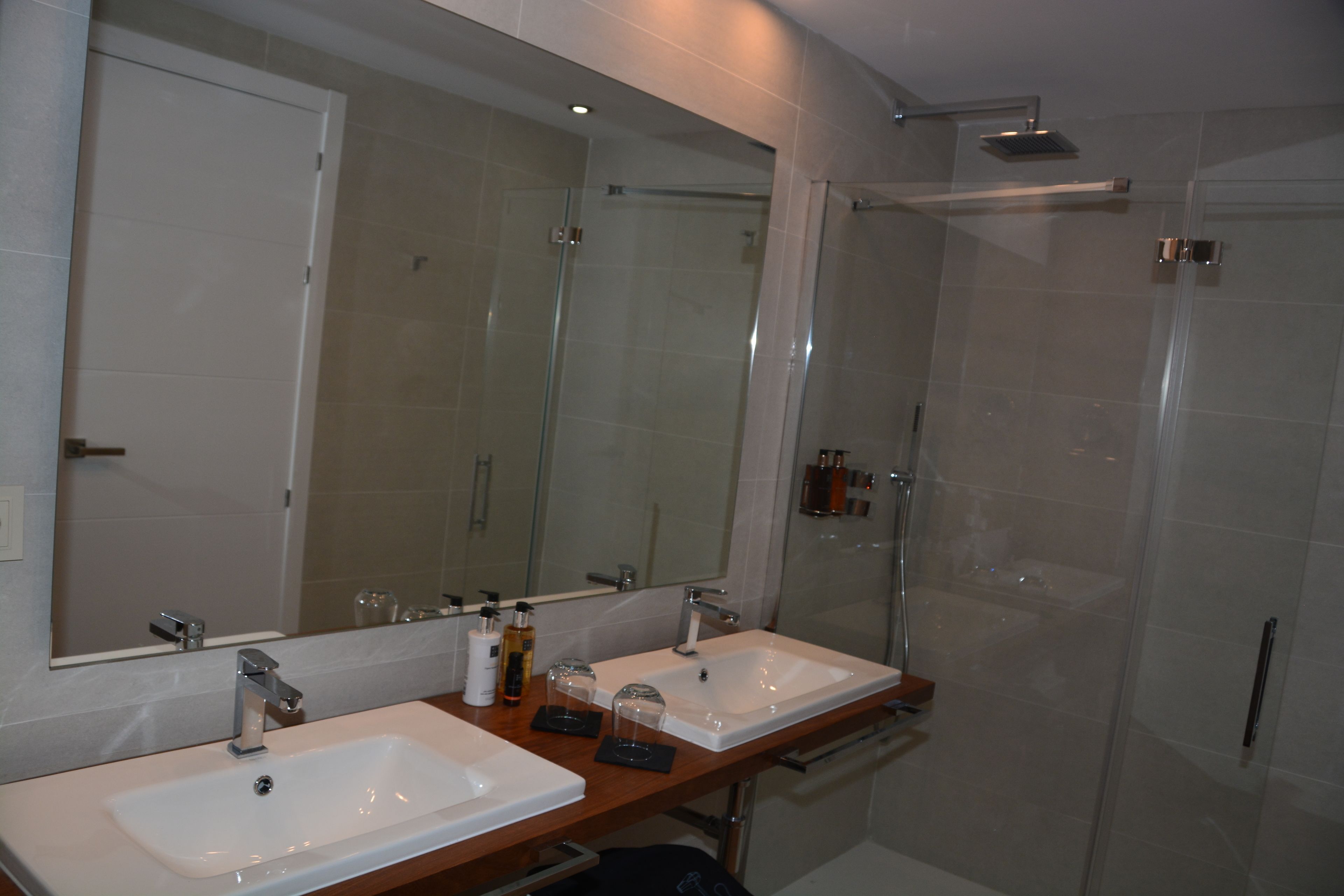 Un baño moderno con dos lavabos, un espejo grande y una ducha con mampara de vidrio.