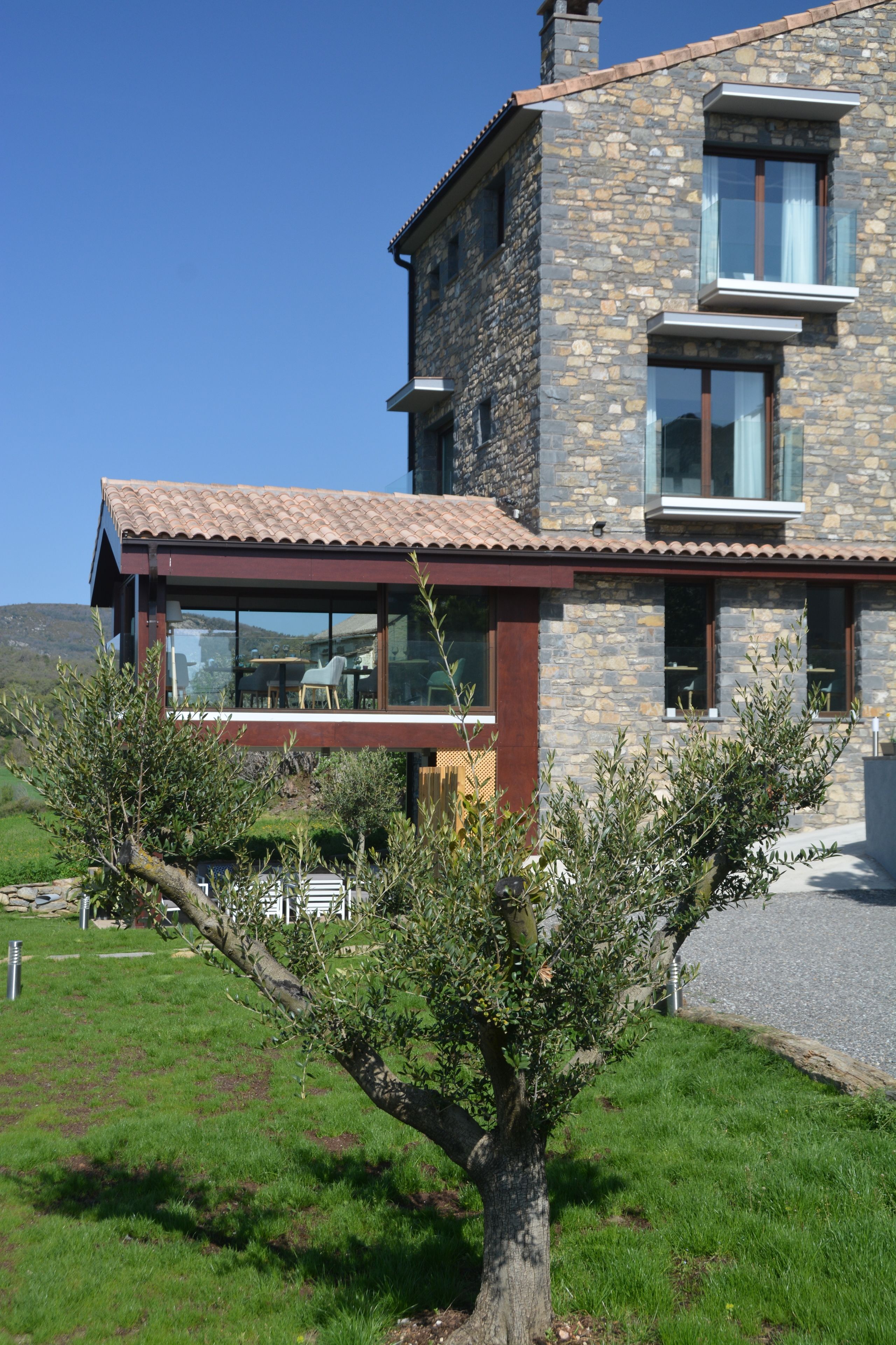 Una casa moderna de dos pisos con fachada de piedra, ventanas amplias y un balcón.