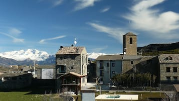 A village with stone buildings, a church with a bell tower, and snow-capped mountains in the background.