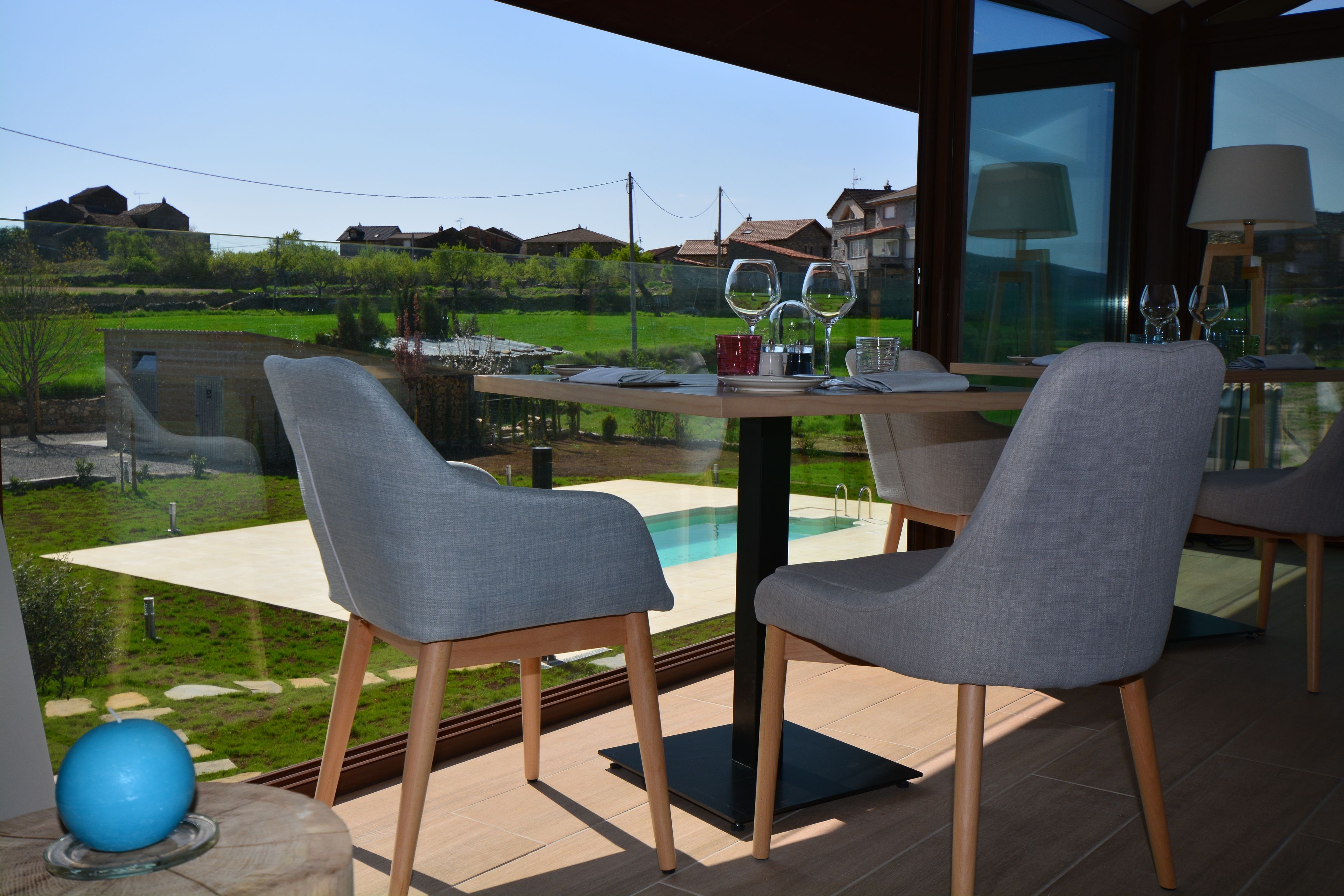 A dining area with a table set for two, overlooking a pool and a green landscape.
