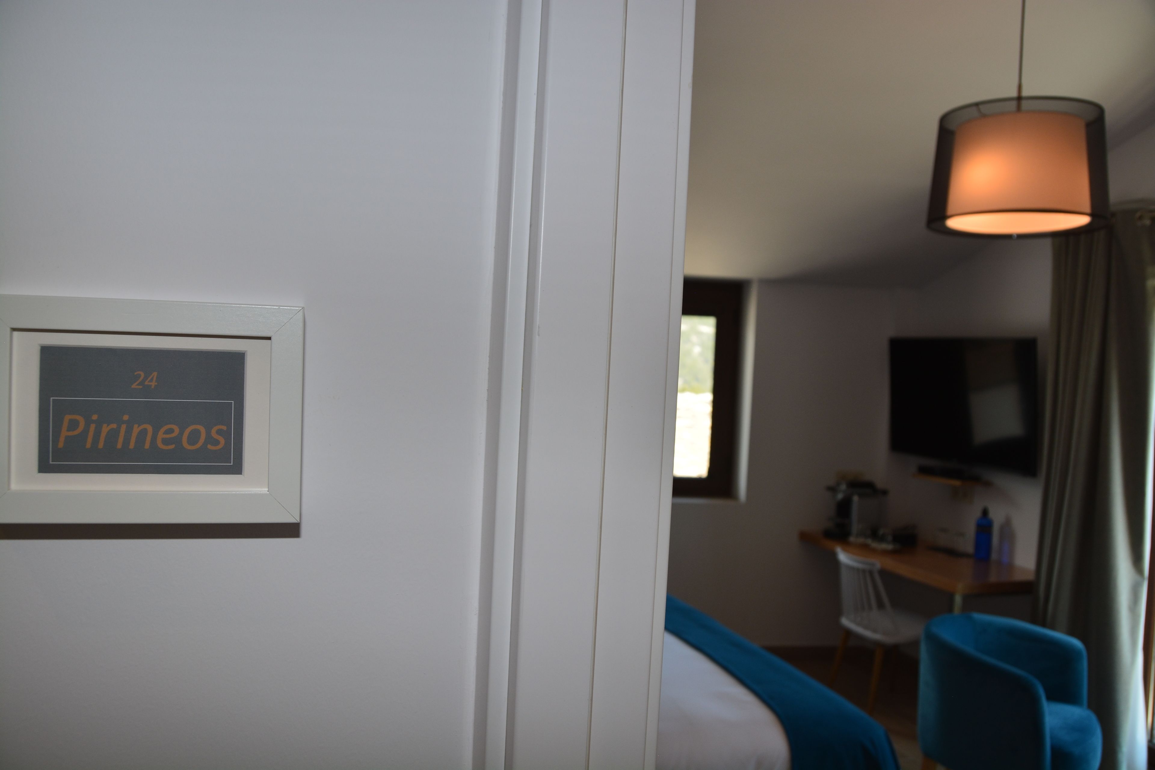 A hotel room with a framed sign on the wall, a desk with a chair, a television mounted on the wall, and a blue chair.