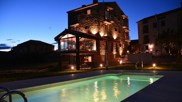 Ein Steinhaus mit Pool davor, inklusive überdachter Terrasse und Sitzgelegenheiten im Freien.