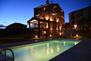 Un bâtiment en pierre avec une piscine à l’avant, doté d’un patio couvert et d’un espace salon extérieur.